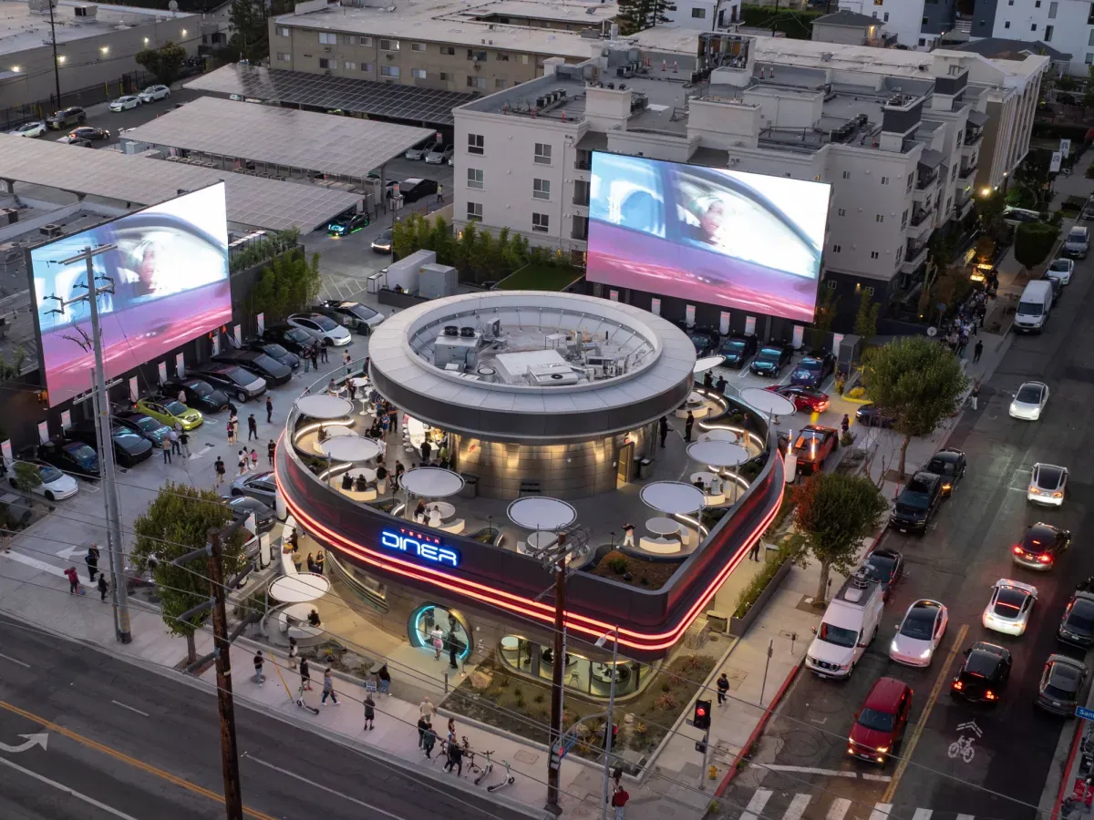 The Tesla Diner in Hollywood at dusk, cars charging under two large outdoor screens